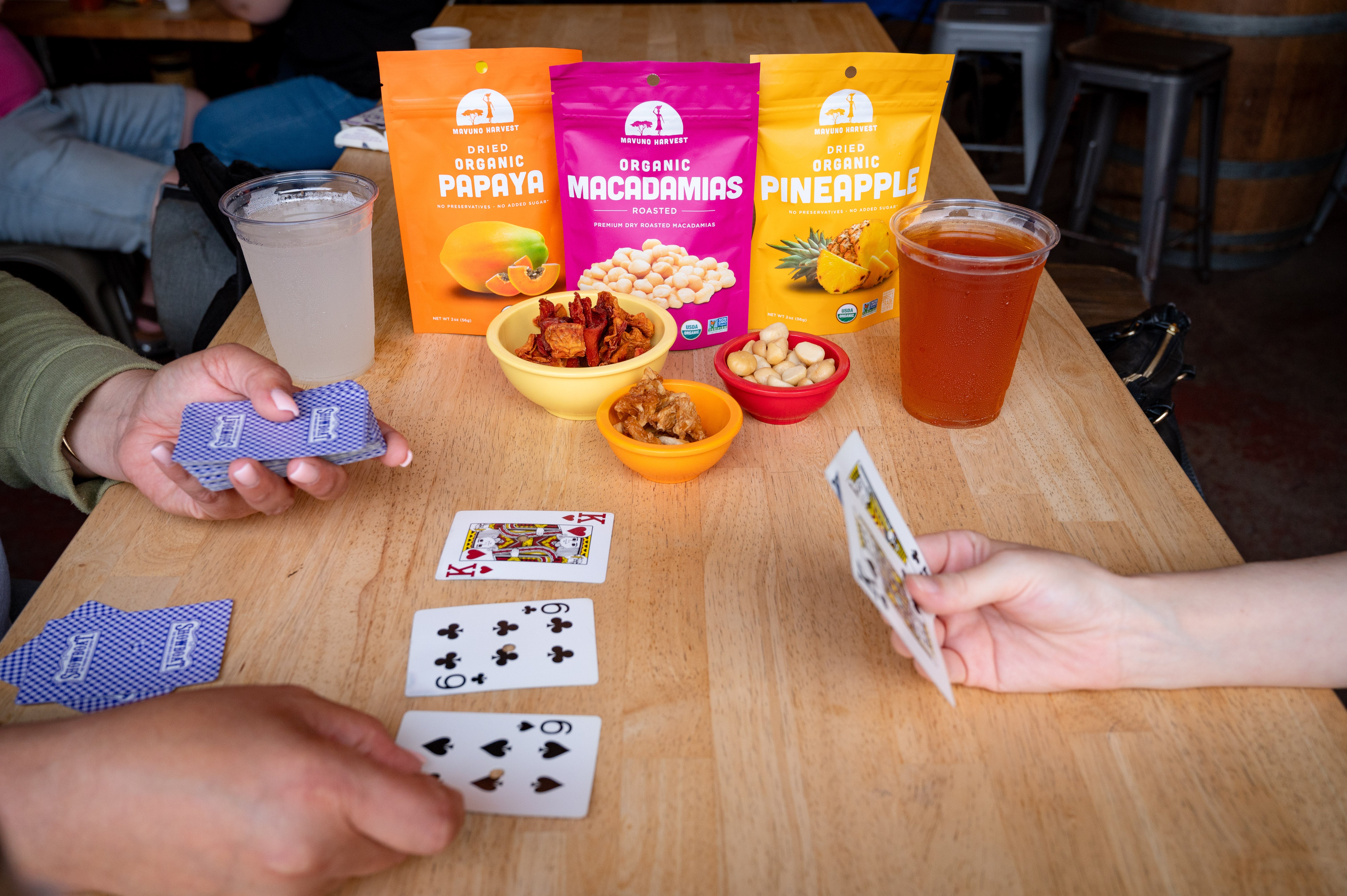 People playing cards and sharing Mavuno snacks at a table