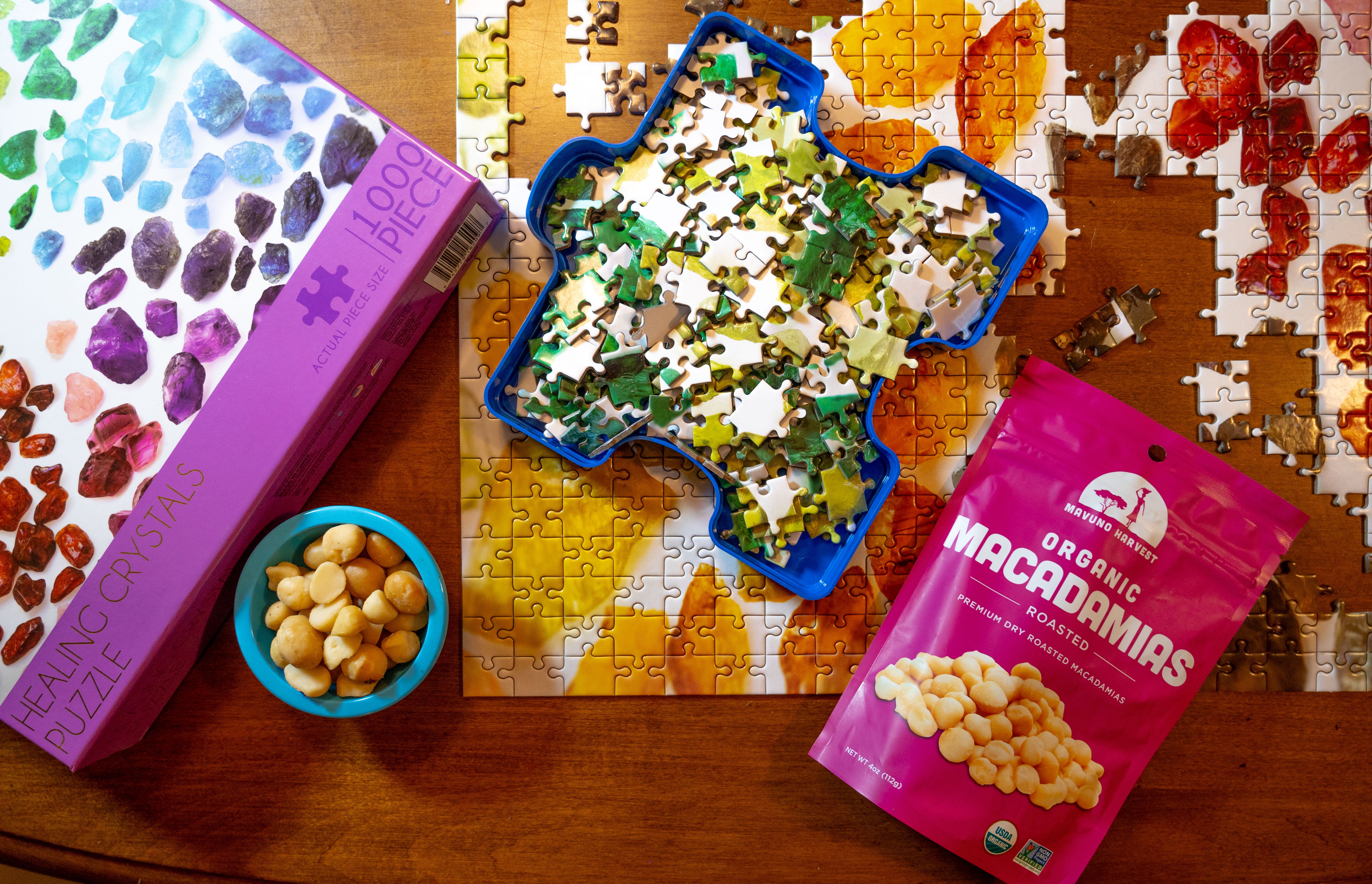 Mavuno roasted macadamias beside a bowl of nuts and a puzzle on a table